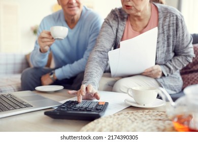 Close-up Of Married Senior Couple Sitting At Coffee Table And Using Calculator While Thinking How To Save Money