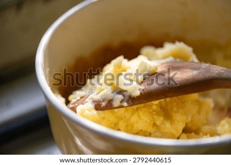 Close-up of mashed potatoes in a pot, being stirred with a wooden spoon. The focus is on the creamy texture of the potatoes.