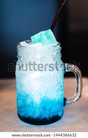 Closeup mason jar glass of cold fresh blue lagoon cocktail with ice on table and blurred dark background.