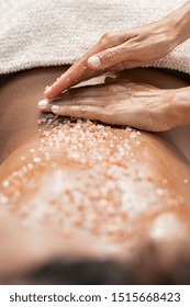 Closeup Of Masseuse Woman Applying Scrub For Peeling On African Woman Back At Spa. Therapist Hands Applying Exfoliation Rock Salt On Girl Back At Wellness Center. Lady Lying For Body Treatment Therapy