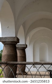 Close-up of massive stone columns supporting white arches in a historic building, showcasing classical architectural design and craftsmanship.