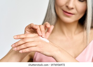 Closeup. Mature Beautiful Senior Mid Age Older Asian Woman Of 50s Years Applying Putting Skin Care Lotion Hand Cream Doing Her Everyday Routine. Antiaging Beauty Skin Face Body Care Concept.