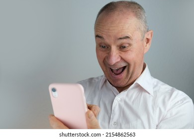 close-up of mature charismatic man looks at screen of phone in pink cover, senior 60 years laughs merrily, smiles openly, rejoices at good news, concept funny unexpected, good mood, optimism