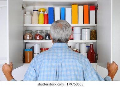 Closeup of a mature male looking into his pantry, The cupboard is full of groceries. The man is seen from behind and is unrecognizable.