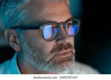 Close-Up Of Mature Man With Glasses Focused On Computer Screen, Reflections In Lenses, Dim Lighting, Late Night Work, Technology And Concentration - Powered by Shutterstock