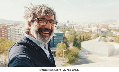 Close-up of mature man taking selfie while standing on balcony, looks at camera - Powered by Shutterstock