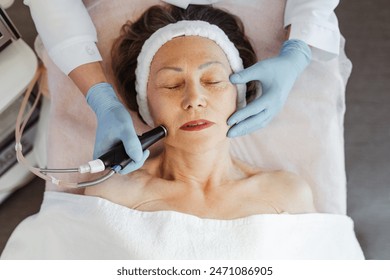 Close-up of mature woman getting facial hydro microdermabrasion peeling treatment at cosmetic beauty spa clinic, top view. Rejuvenation, cosmetology concept - Powered by Shutterstock