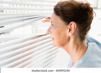 Close-up of mature woman looking through blinds - Powered by Shutterstock