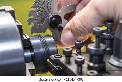 Close-up of measurement by thread pitch gauge. Detail of a machinist's hand with the set of threaded gauges. Threading by a steel tool bit on a lathe. Idea of machining, metalworking, engineering.