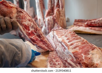 close-up of meat processing in the food industry, the worker cuts raw pig, storage in refrigerator, pork carcasses hanging on hooks in a meat factory - Powered by Shutterstock