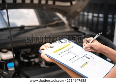 Close-up at a mechanic foreman's hand is checking on multi-point car service guideline checklist form, to verify the car service quality. Expertise working action scene, selective focus.