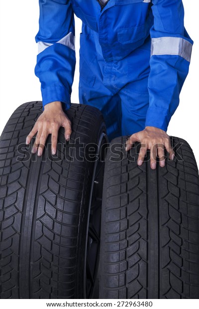 Closeup of mechanic hands with blue uniform holding\
two tires, isolated on\
white