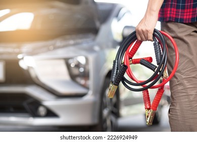 
Close-up of mechanic holding car battery jumper cable when experiencing dead battery in garage battery extension cable car maintenance service concept