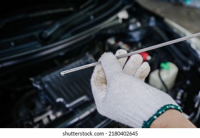 Close-up of mechanic is holding the oil dipstick to check the engine oil level. top view hand of a man wearing white gloves holding a dipstick to check and maintain the engine, check engine oil level - Powered by Shutterstock