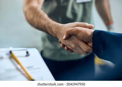 Close-up of mechanic and maintenance engineer shaking hands at car workshop. 