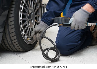 Closeup Of Mechanic At Repair Service Station Checking Tyre Pressure With Gauge - Powered by Shutterstock