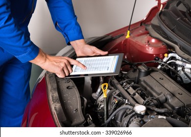 Close-up Of Mechanic Using Digital Tablet While Examining Car Engine In Garage - Powered by Shutterstock