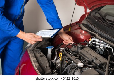 Close-up Of Mechanic Using Digital Tablet While Examining Car Engine In Garage - Powered by Shutterstock