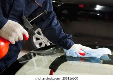 Close-up Of Mechanic Working In Auto Repair Shop: Cleaning The New Car Windshield