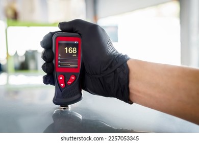 Close-up of a mechanic's hand holding a magnetic thickness gauge. Instrument for measuring paint thickness. Checking a car at a service station - Shutterstock ID 2257053345