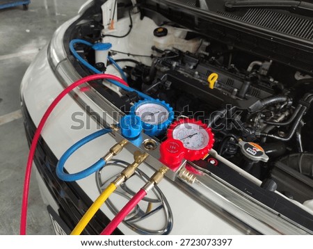 A close-up of a mechanic's hands checking and refilling the refrigerant and recharging a car's AC. A worker is repairing a car's AC.