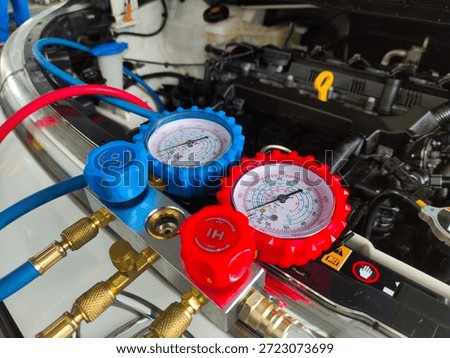 A close-up of a mechanic's hands checking and refilling the refrigerant and recharging a car's AC. A worker is repairing a car's AC.