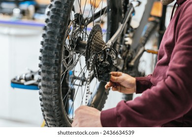 Close-up of the mechanic's hands on the wheel of a mountain bike, with focus centered on the chain - Powered by Shutterstock