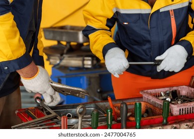 Close-up of mechanics' hands selecting tools in a garage. wrenches and screwdrivers. Male and female technicians in yellow and blue uniforms working with equipment. Precision in auto repair tasks. - Powered by Shutterstock