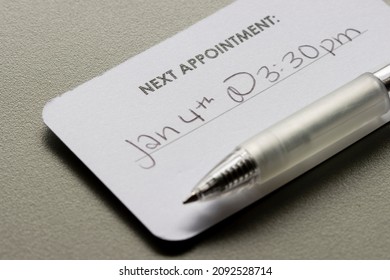 Closeup Of A Medical Appointment Reminder Card With Hand-written Date And Time Isolated On A Gray Background.