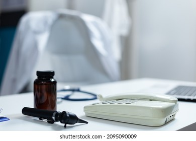 Closeup Of Medical Otoscop And Landine Standing On Table In Empty Doctor Office Ready For Clinical Examination. Hospital Room With Nobody In It Equipped With Professional Tools. Medicine Concept