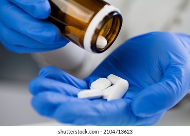 Closeup of medical worker or pharmacist hands wearing blue latex protective gloves,pouring white medicine pills on palm of hand,Coronavirus therapy treatment illustration,cure for COVID-19 new variant