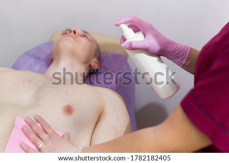 Close-up of mens Breasts in the beauty salon for the procedure of sugar hair removal. Beautician sprays disinfectant solution on the man's chest. Sugaring