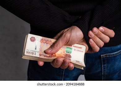 Close-up of men's hands holding a bundle of Russian money with five thousand bills behind their backs. Corruption, bribes.