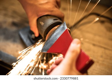 Close-up of men's hands sharpening an axe on an electric sharpener. Repair of home tools. 
Sparks fly.