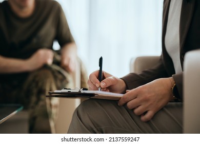 Close-up Of Mental Health Professional Writing Notes While Having Meeting With A Veteran.