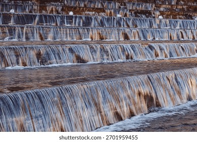 Close-up of a mesmerizing tiered waterfall featuring water cascading over multiple steps. Shimmering liquid creates a soothing, dynamic pattern, reflecting natural light for calm and serene aesthetic.