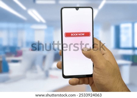 Close-up of the “Book Now” message on the smartphone screen. Online booking concept. Office background. Early booking message.
