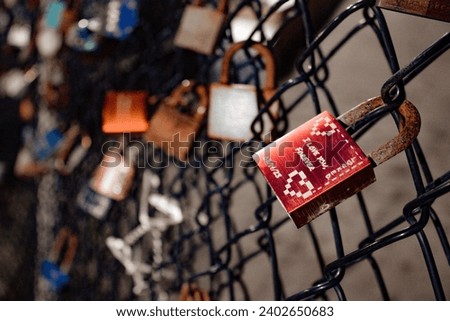 A close-up of a metal chain-link fence with a variety of padlocks attached to it, secured tightly in place