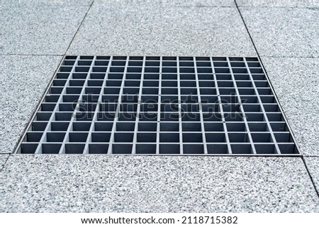 Close-up, metal cover of street water drain. Against the background of paving slabs of gray granite