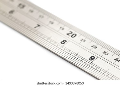 Close-up Of A Metal Ruler Showing Inches And Centimetres, Laid Flat On A White Backdrop, With The Number 9 In Focus With A Shallow Depth Of Field