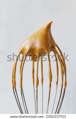 close-up of Metal whisk with whipped coffee for dalgona coffee drink isolated on the white background. vertical. the whisk with whipped cream with copy space