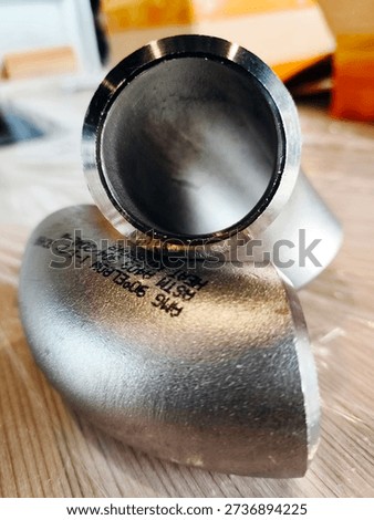 Close-up of a metallic pipe elbow fitting on a wooden surface, showing industrial details and engraved markings