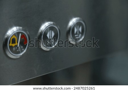 a close-up of a metallic surface with three circular buttons. Each button features different icons: an elevator emergency button, open button, and close button.