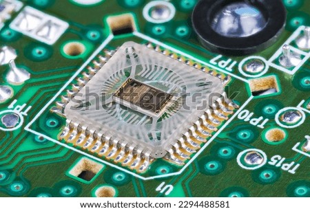 Closeup of microchip die inside optical sensor on green printed circuit board. Electronic square transparent surface mounted component to detect motion and round light source on PCB in computer mouse.