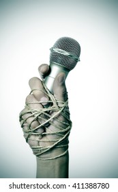 Closeup Of A Microphone In The Hand Of A Young Man Tied With Rope, Depicting The Idea Of The Repression Of The Mass Media Or The Lack Of The Freedom Of Speech