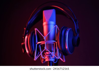 A close-up of a microphone and headphones for podcasting or ASME sounds on black stand in a neon led lighting, cyan and magenta, in a sound recording studio - Powered by Shutterstock