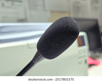 A close-up of a microphone of an intercom system with a black foam cover, set against a blurry office background featuring paperwork and computer equipment.

 - Powered by Shutterstock