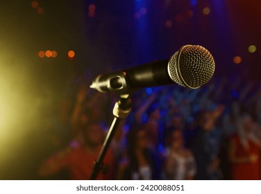 Closeup, microphone and stage performance in theater with audience and sound equipment for concert or singing. Audio, technology and light in dark room with crowd for open mic, karaoke or music event