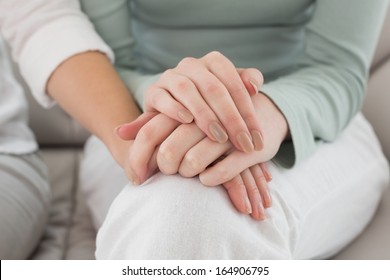 Close-up mid section of female friends touching hands at home on the couch
