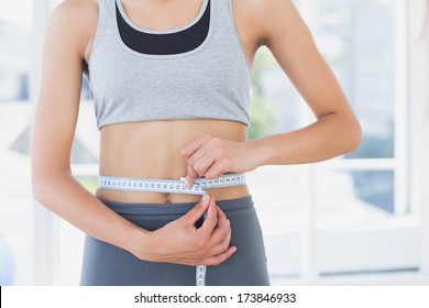 Closeup mid section of a sporty young woman measuring her waist in the fitness studio